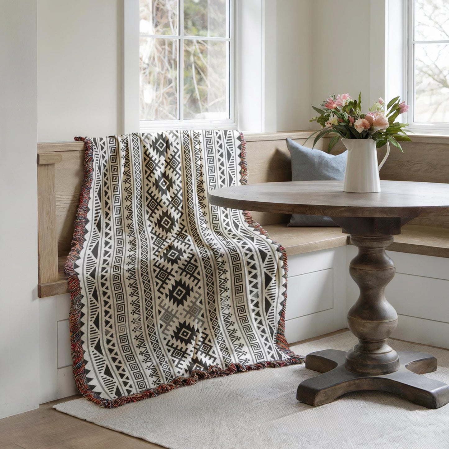a cozy corner with a wooden table, a bench, and a decorative throw blanket with a geometric pattern. A vase of flowers is placed on the table, adding a touch of nature to the scene. The overall atmosphere is warm and inviting, with the wooden furniture and the colorful accents creating a harmonious and visually appealing space.