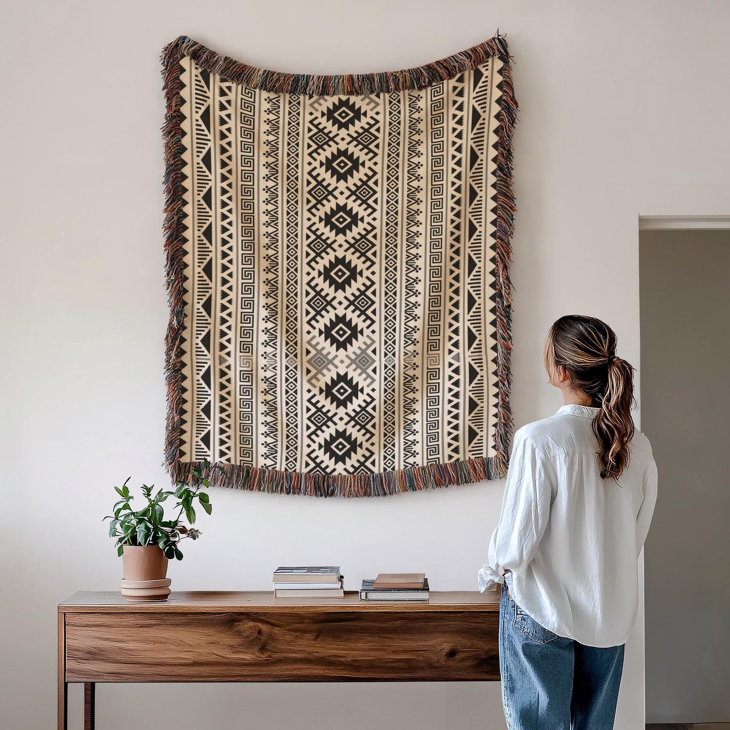 A woman stands in front of a wooden console table, looking up at a large, colorful tapestry hanging on the wall above it.