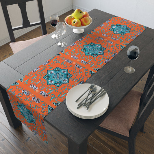 Orange and turquoise Armenian alphabet table runner on a dining table with wooden chairs and a bowl of fruit