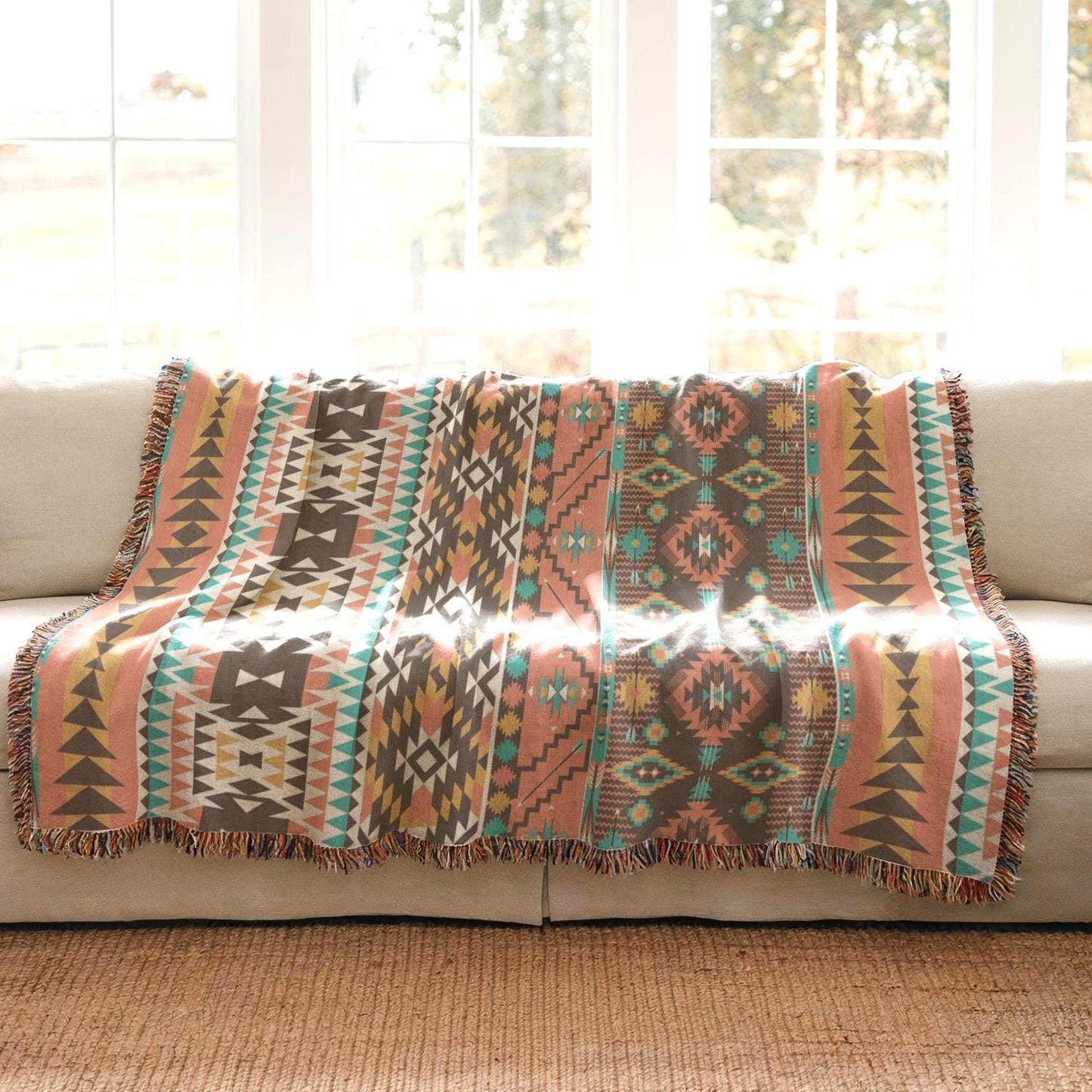 a colorful, patterned throw blanket draped over a beige couch, with a window in the background.