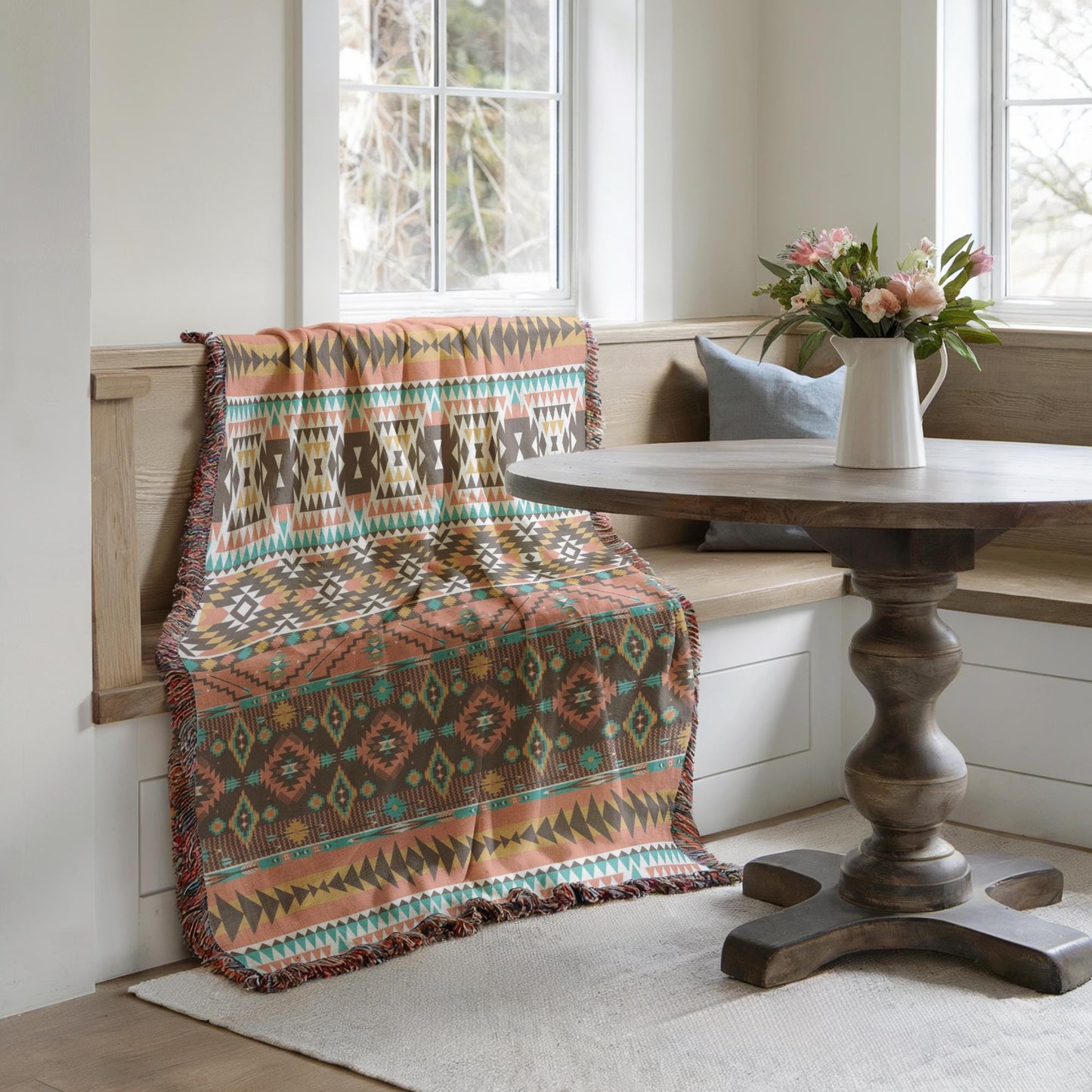 a cozy corner with a wooden table, a colorful throw blanket draped over the back of the bench, and a vase of flowers on the table.