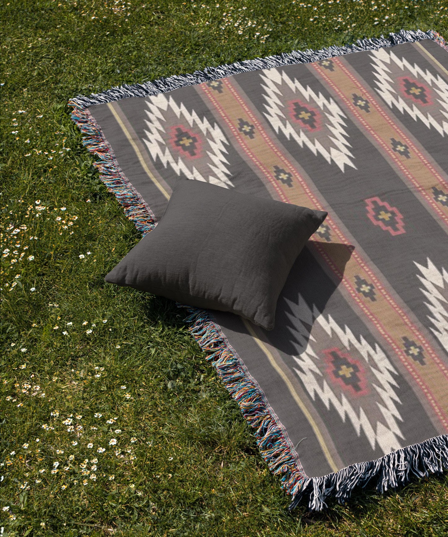 a gray throw pillow resting on a colorful, patterned blanket spread out on a grassy lawn.