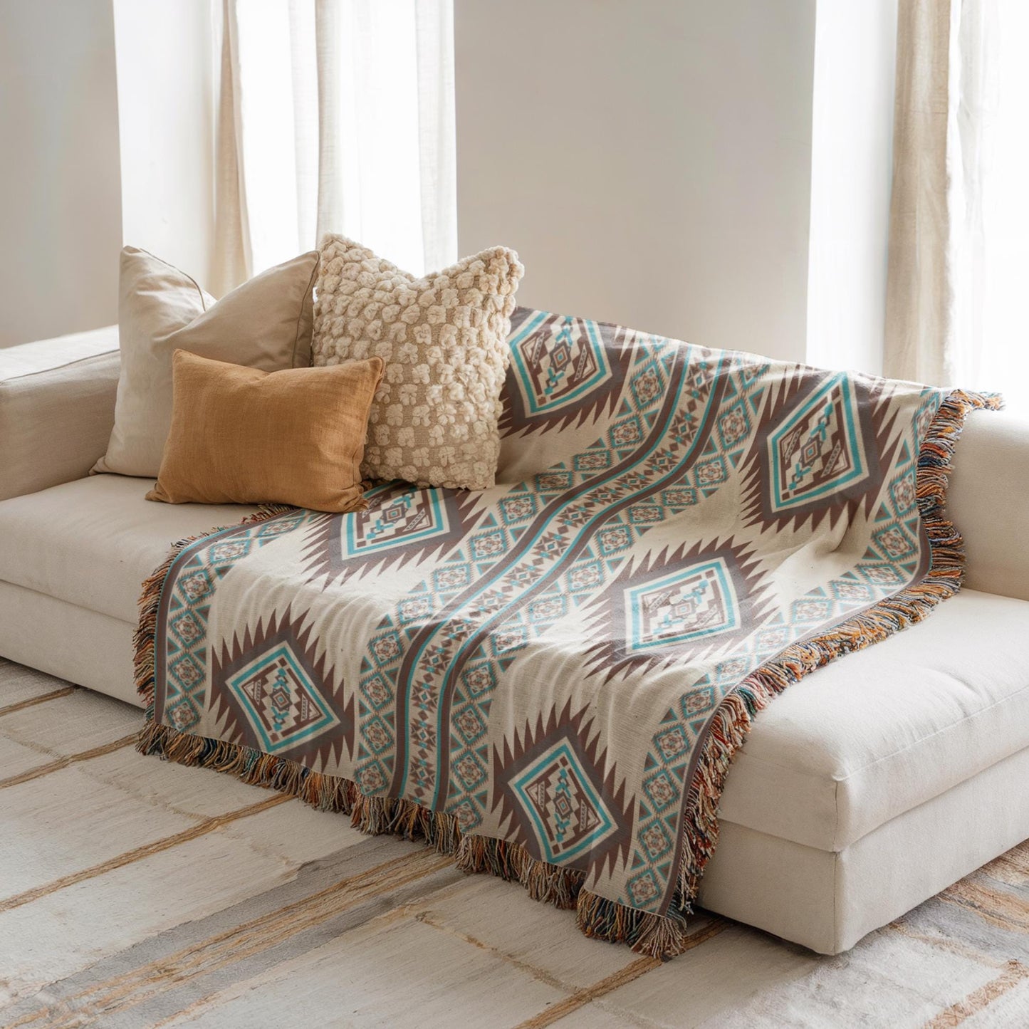 a cozy living room with a white sofa adorned with a patterned throw blanket and three decorative pillows. The pillows have a mix of neutral and vibrant colors, creating a visually appealing and inviting atmosphere.