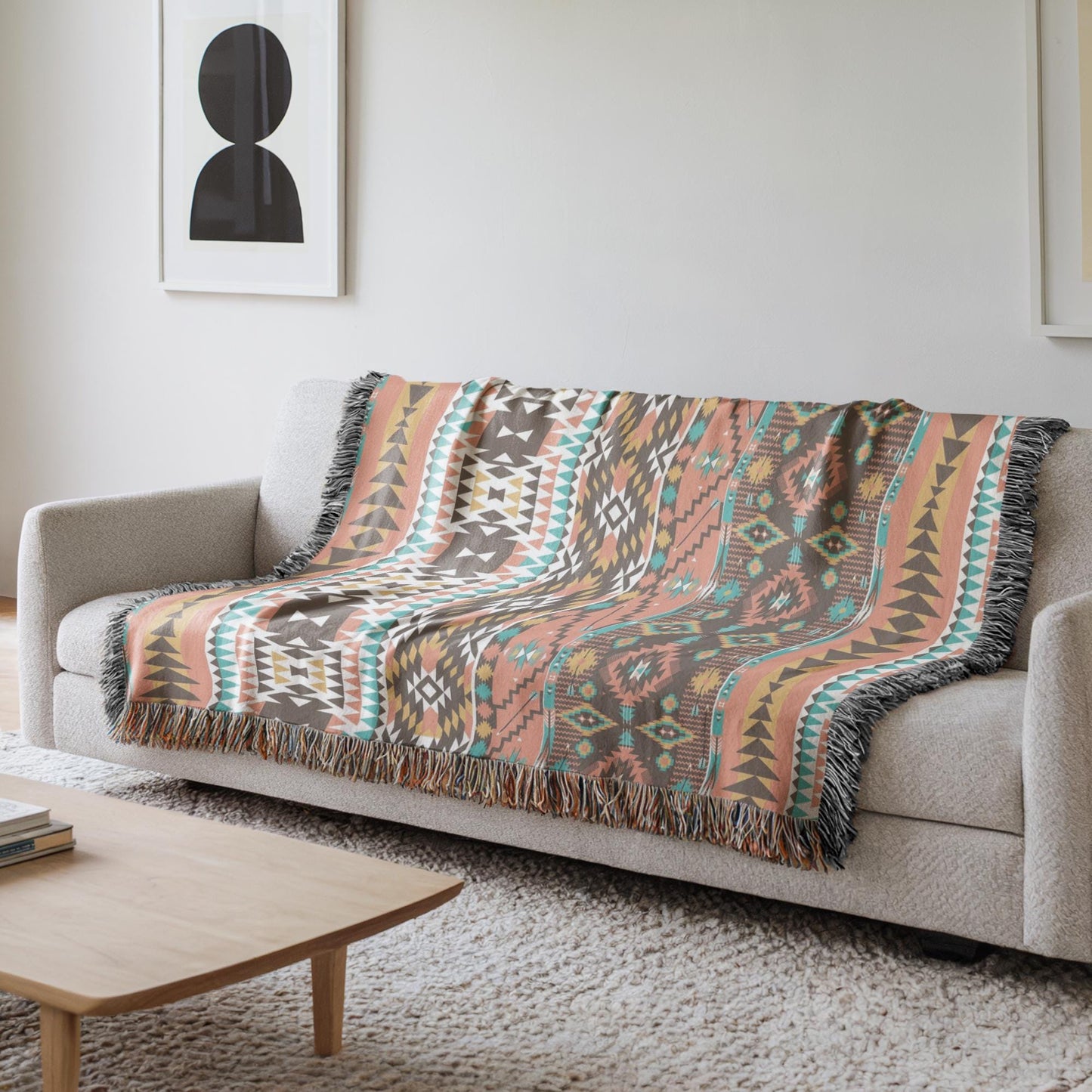 a cozy living room with a gray sofa and a wooden coffee table. A colorful, patterned throw blanket is draped over the sofa, adding a vibrant touch to the room. The room has a minimalist and modern design, with a white wall and a framed picture hanging above the sofa.