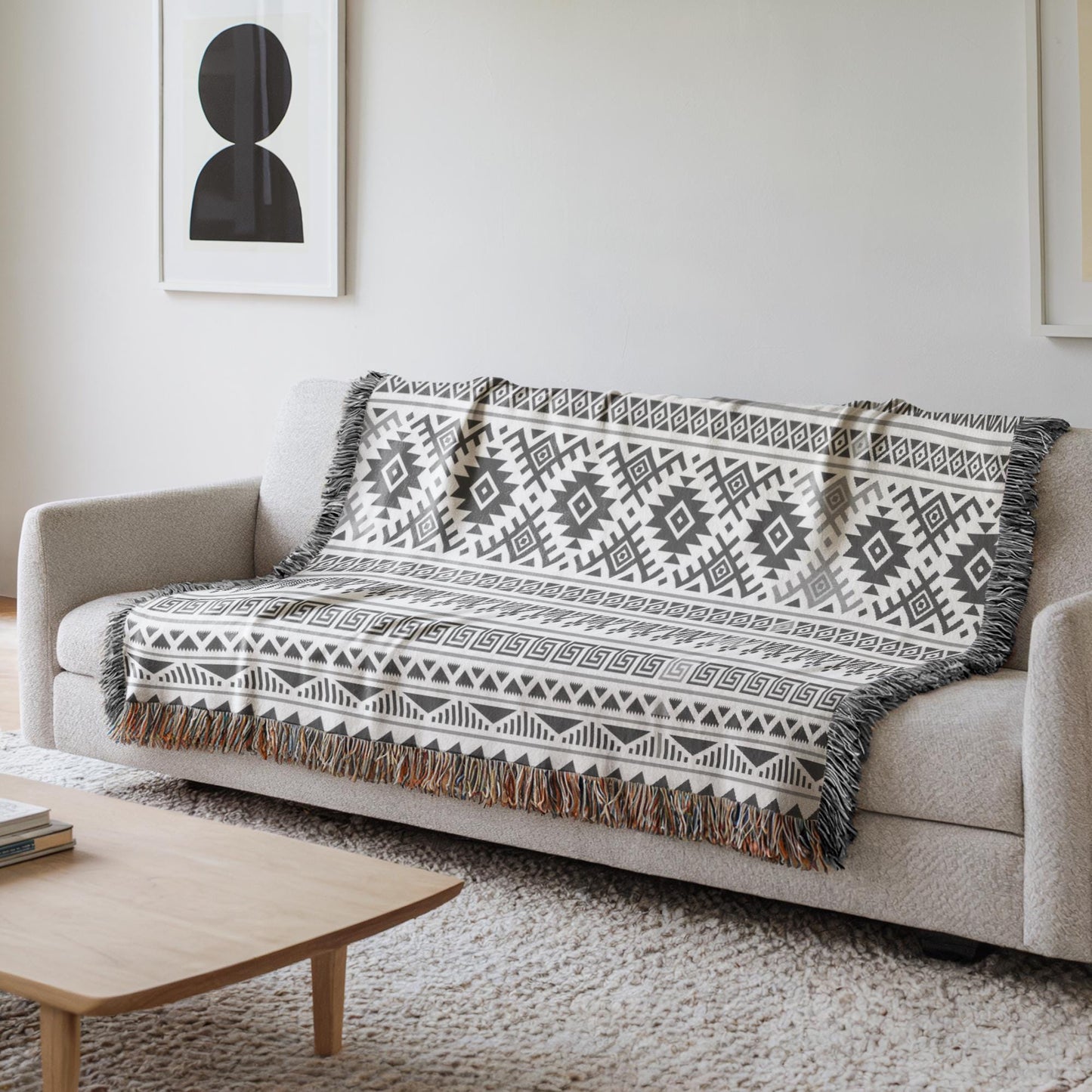 a cozy living room with a gray sofa adorned with a patterned throw blanket. The blanket has a geometric design in black and white, adding a touch of elegance to the space. In the background, there is a framed picture hanging on the wall, and a wooden coffee table is placed in front of the sofa.
