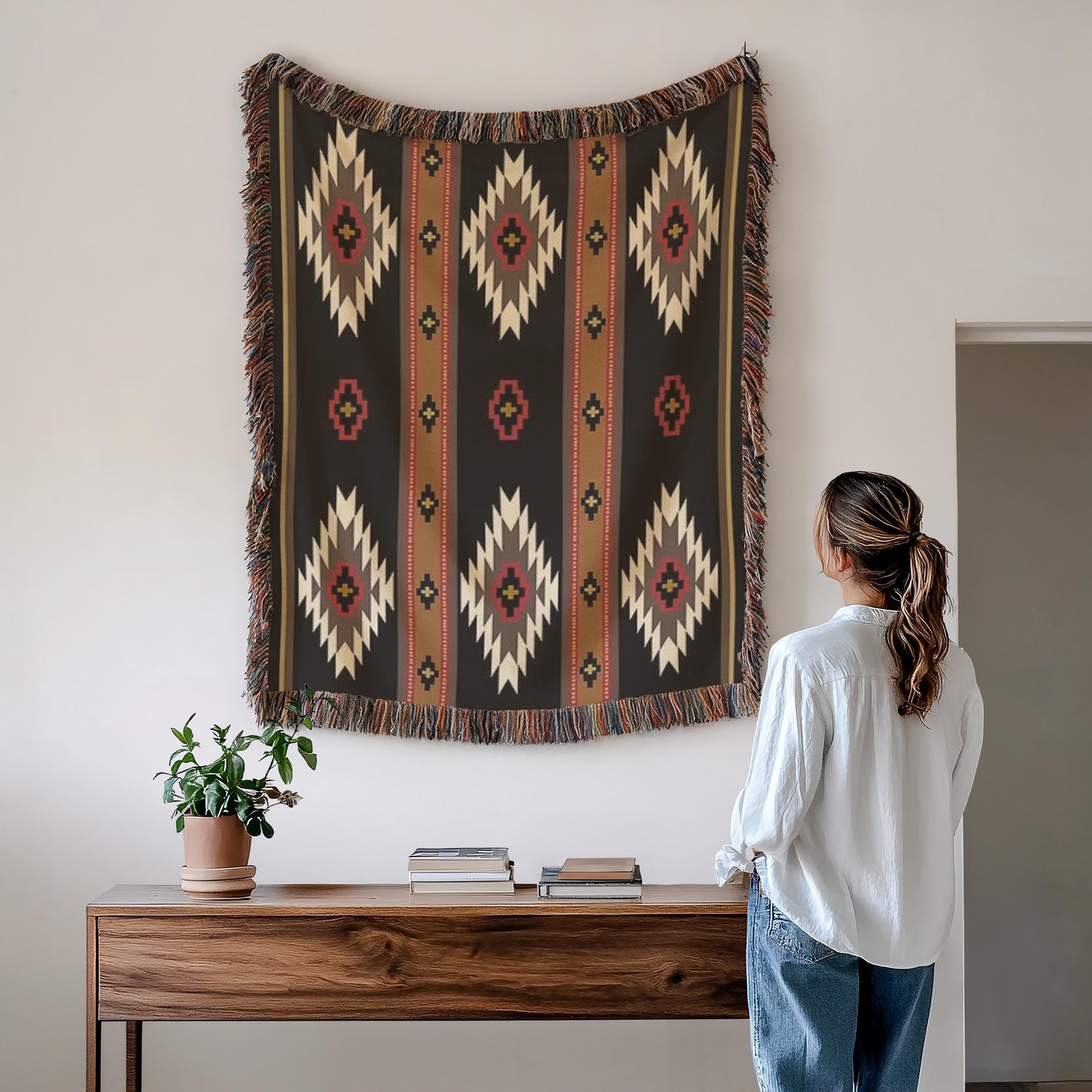 A woman stands in front of a wooden table, looking at a large, colorful tapestry hanging on the wall above it.