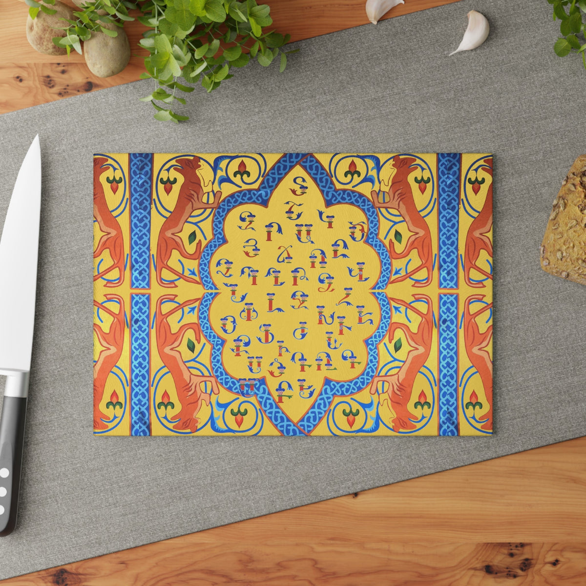 Yellow and blue Armenian alphabet cutting board on a grey mat beside a knife and fresh herbs