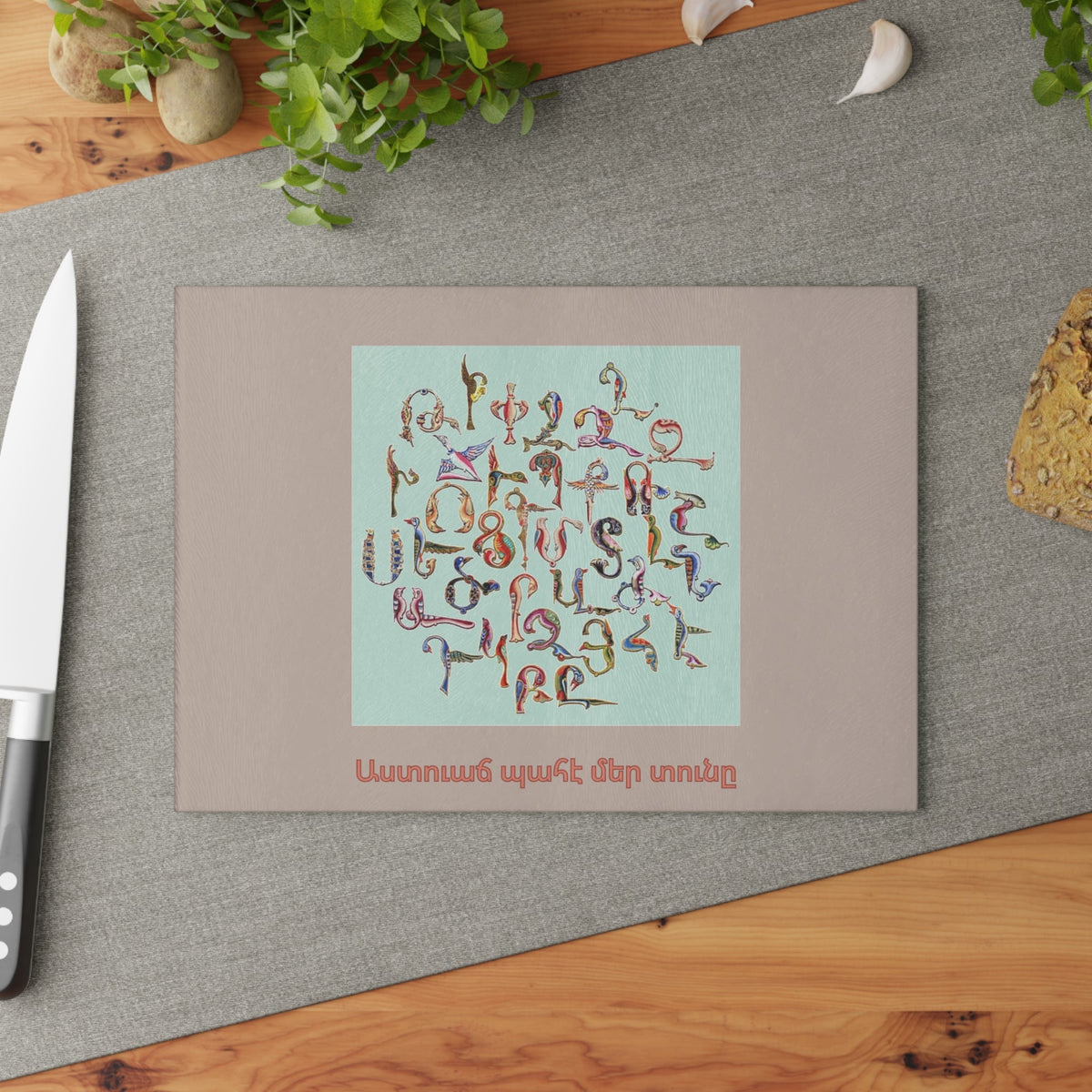 Trchnakir bird letter alphabet cutting board on a grey mat beside a knife and fresh herbs