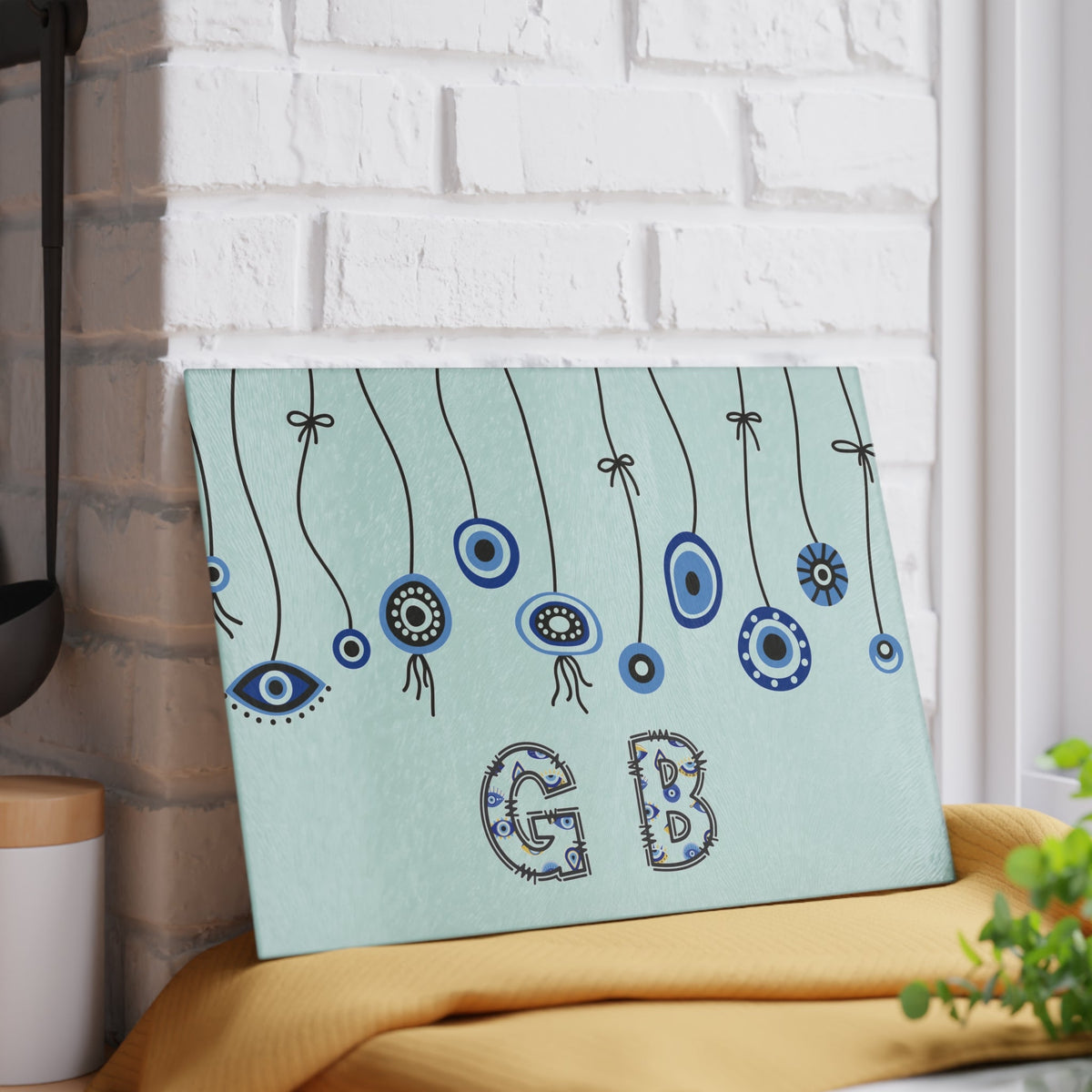 Mint evil eye cutting board with hanging beads angled on a grey mat with a knife and garlic