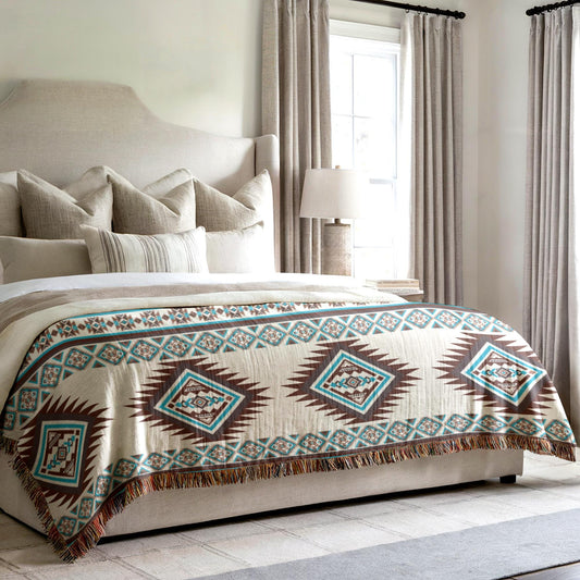 a cozy bedroom with a large bed featuring a patterned blanket and pillows. The bed is positioned against a wall with a window, and there is a lamp on a side table next to the bed.