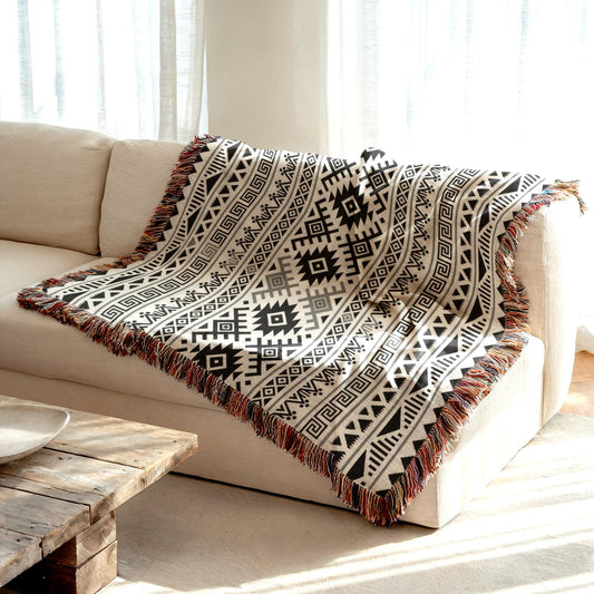 a cozy living room with a beige sofa and a wooden coffee table. A decorative throw blanket with a black and white geometric pattern is draped over the sofa, adding a touch of warmth and texture to the space.