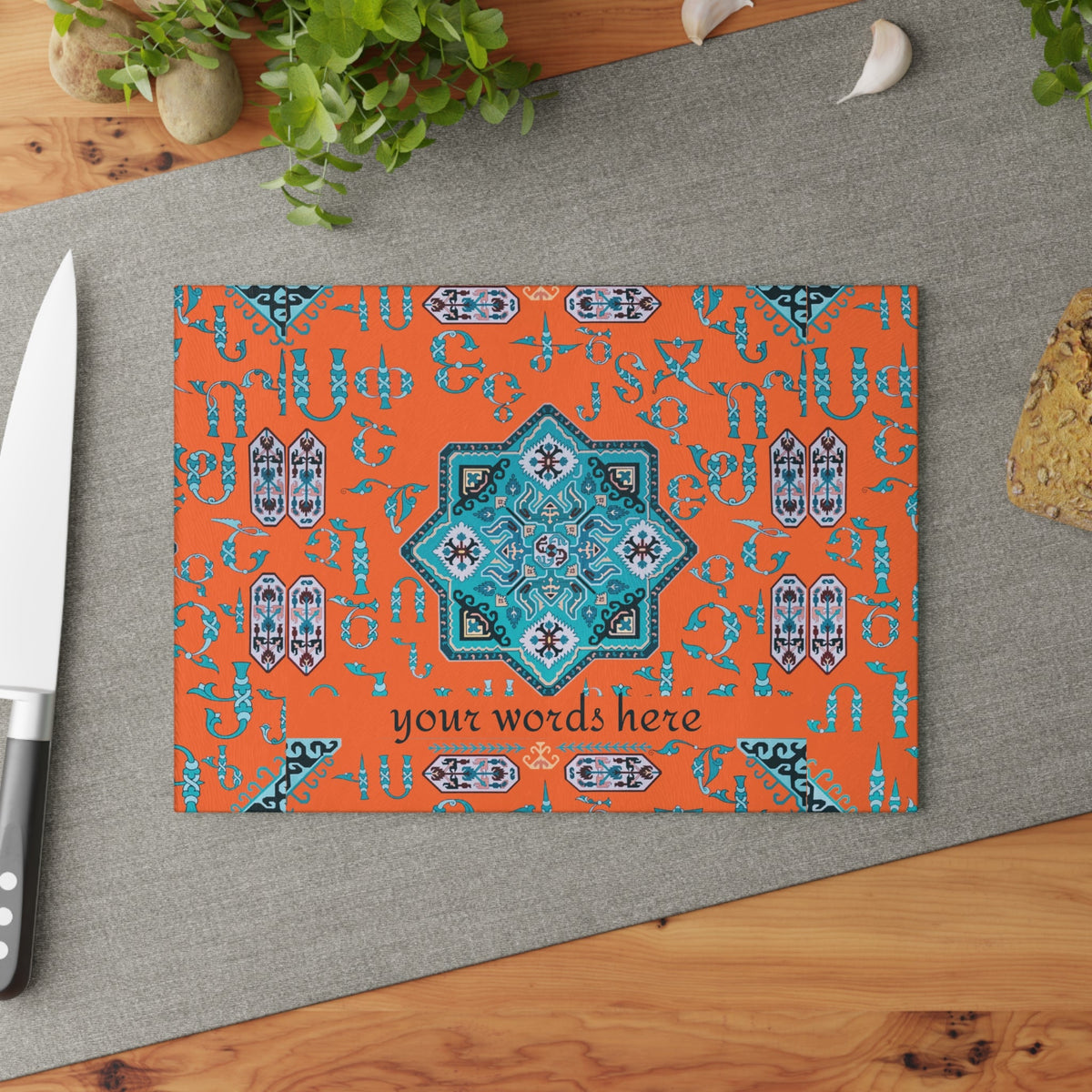 Orange and turquoise Armenian cutting board angled on a grey mat with a knife and garlic