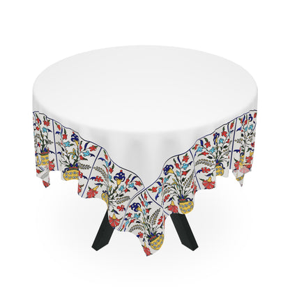 White Armenian tablecloth with floral border on a rectangular table with wooden chairs and house plants