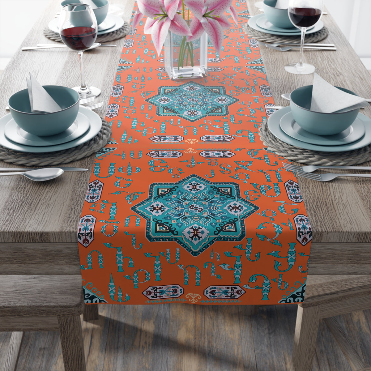 Orange and turquoise Armenian alphabet table runner on a dining table set with white plates and glasses