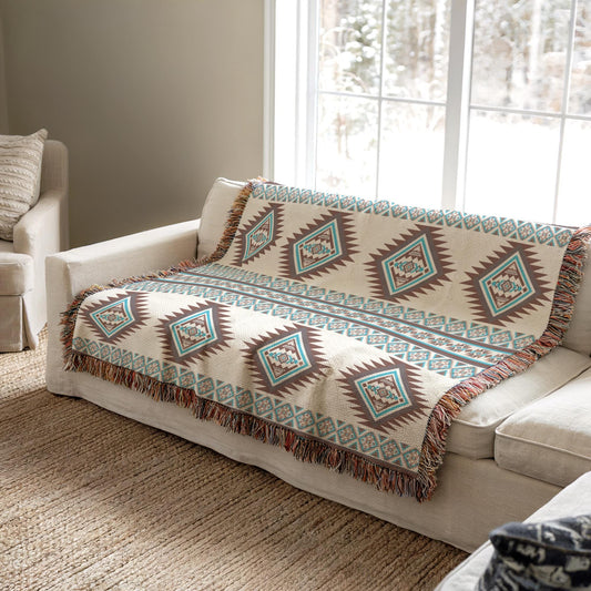 a cozy living room with a white sofa and a patterned throw blanket on it. The blanket has a diamond pattern in shades of blue, green, and brown. The sofa is positioned near a window, allowing natural light to illuminate the room.