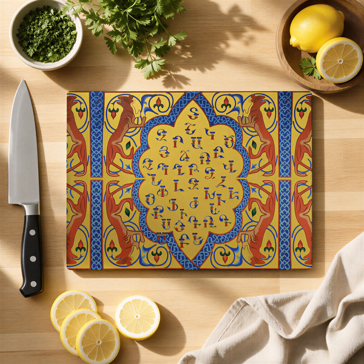 Yellow and blue Armenian alphabet glass cutting board on a wood counter with a knife, lemons and herbs