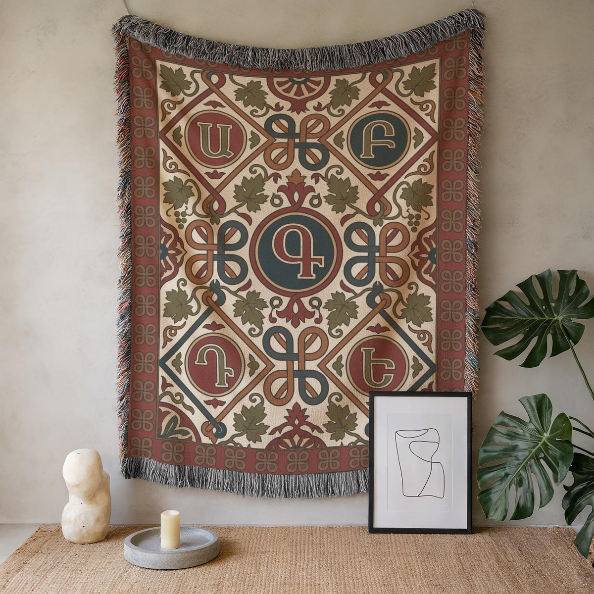 Armenian letter wall tapestry on a plain wall beside a potted plant and small framed art