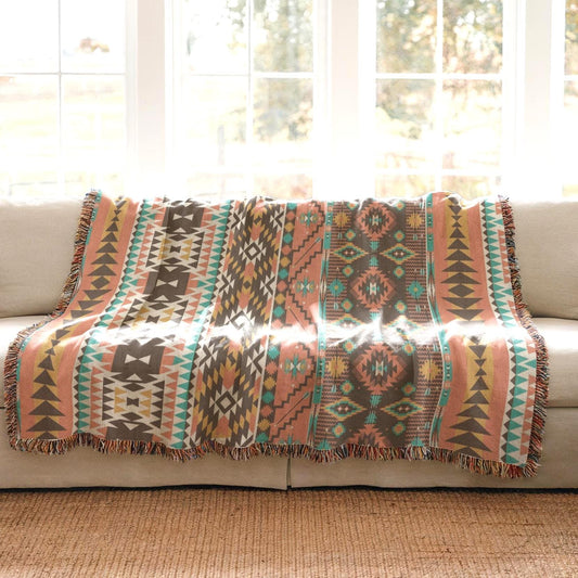 a colorful, patterned throw blanket draped over a beige couch, with a window in the background.