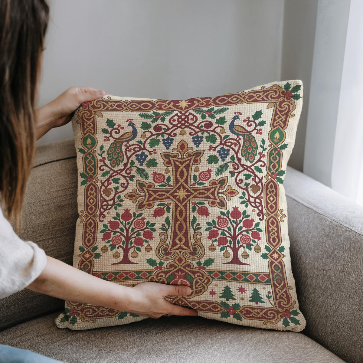 A person is holding a decorative pillow with an intricate, colorful design featuring a cross, trees, and other elements.