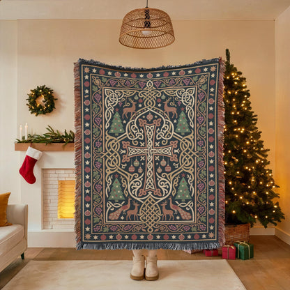 A person stands in front of a Christmas tree, holding a large, intricately patterned blanket with a cross design. The room has a cozy, festive atmosphere with a decorated Christmas tree and a wreath on the wall.