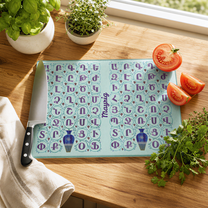 Armenian alphabet glass cutting board with the name Mayrig, on a wood counter with a knife and tomato