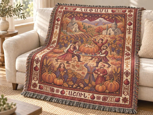 Armenian Ghapama woven cotton blanket draped over a couch, showing a family carrying a stuffed pumpkin, village mountains and a muted burgundy harvest border.