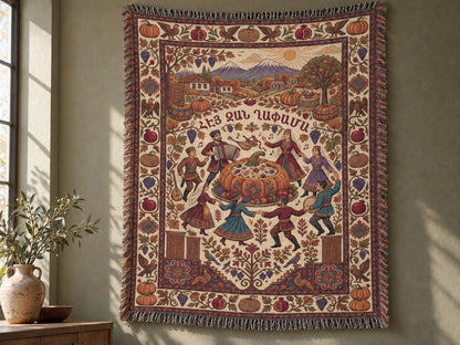 Armenian Ghapama cotton blanket displayed as a wall tapestry, with folk dancers around a stuffed pumpkin, a mountain village and muted burgundy harvest border.