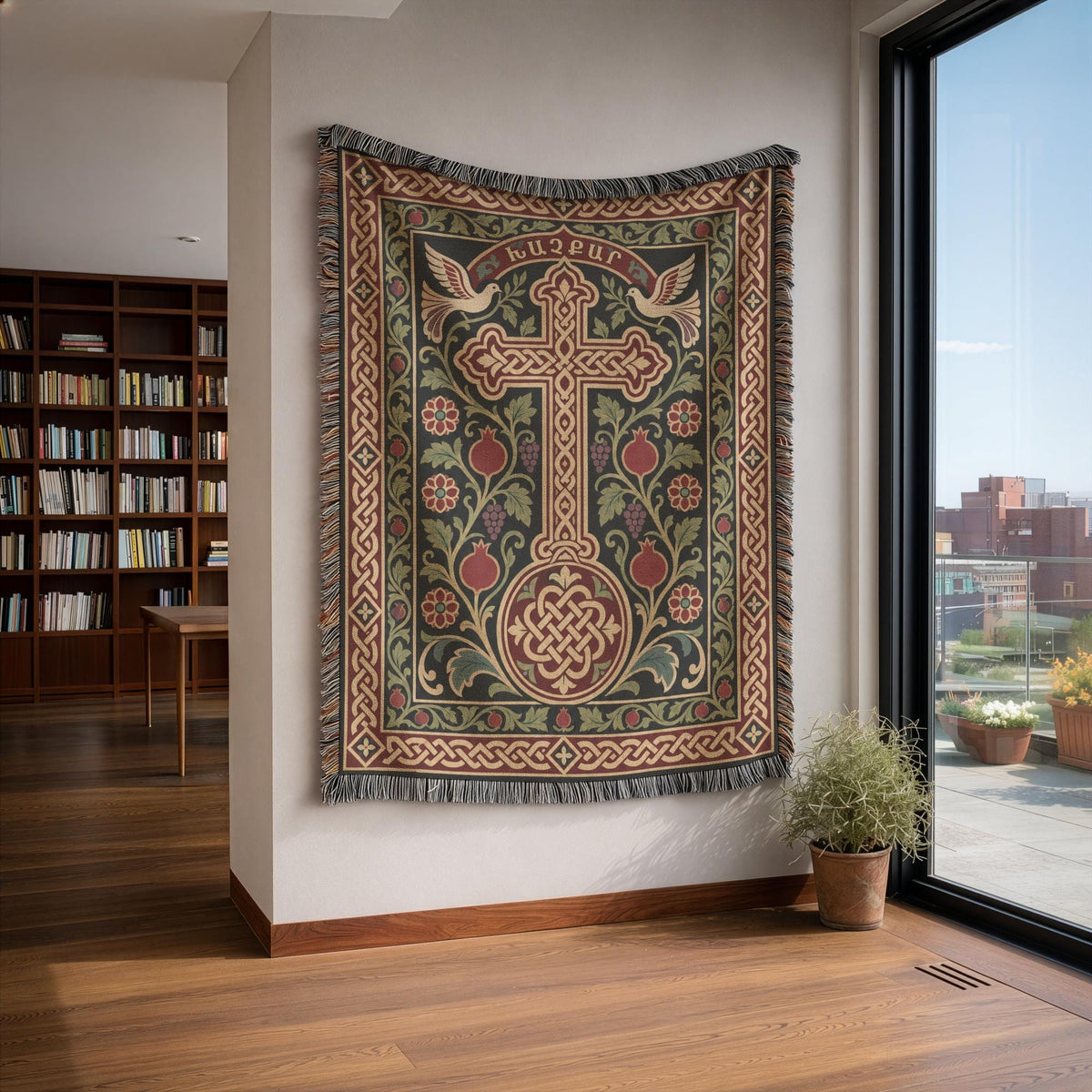 Khachkar tapestry with doves and pomegranates on a white wall beside bookshelves and a tall window