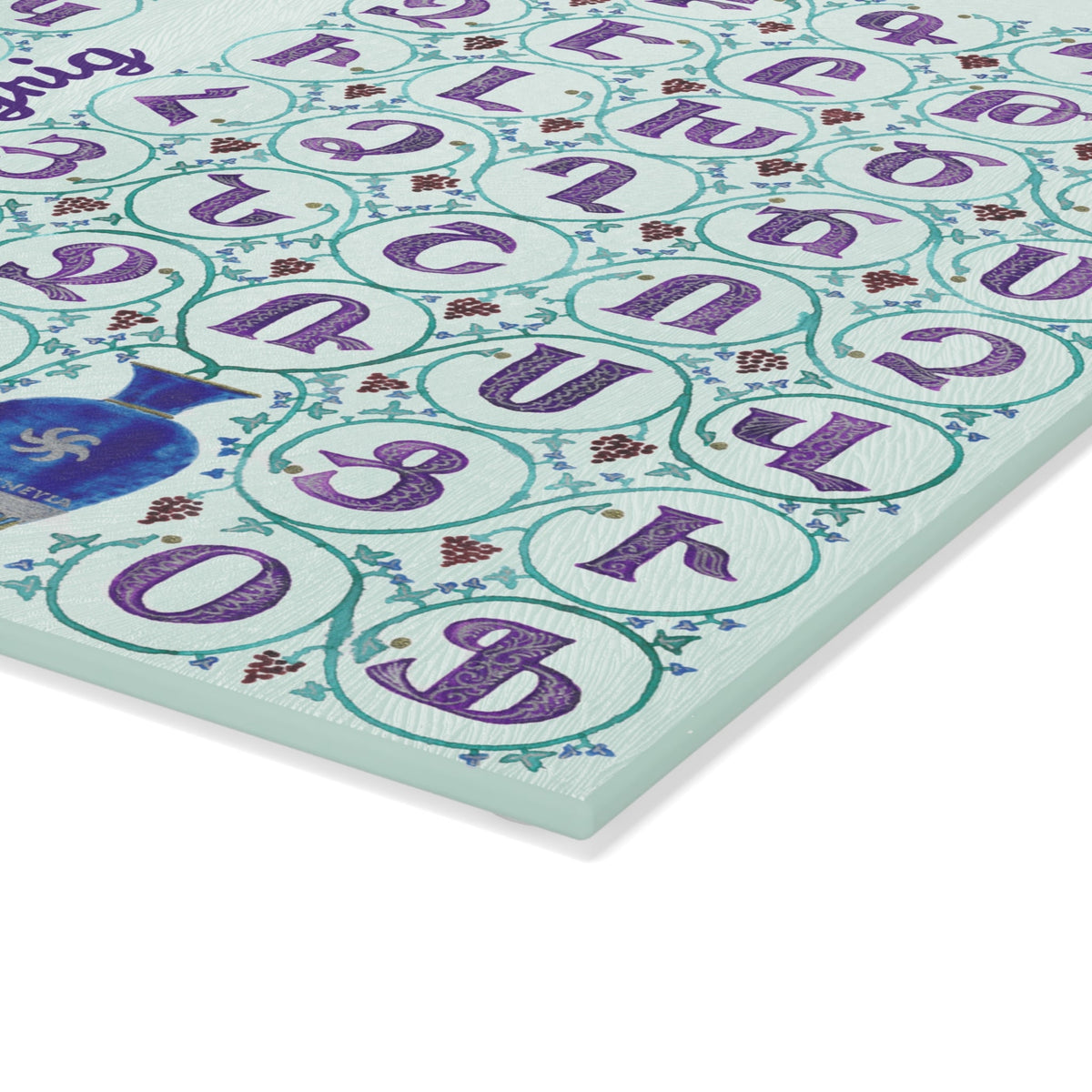 Mint Armenian alphabet cutting board with blue vases angled on a grey mat with a knife and garlic