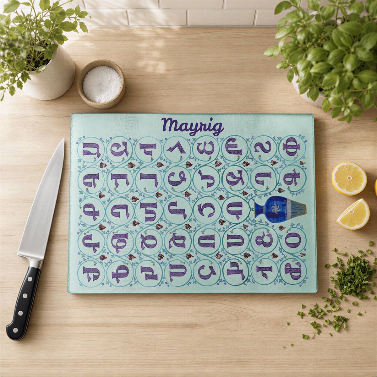 Personalized Armenian alphabet cutting board with the name Mayrig, on a wood counter with a knife and lemons