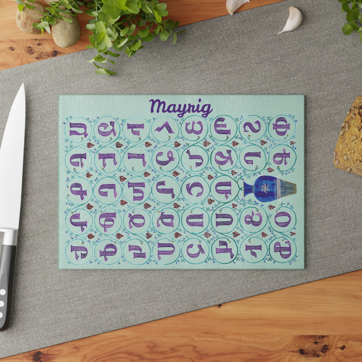 Mint Armenian alphabet cutting board with a name angled on a grey mat with a knife and garlic