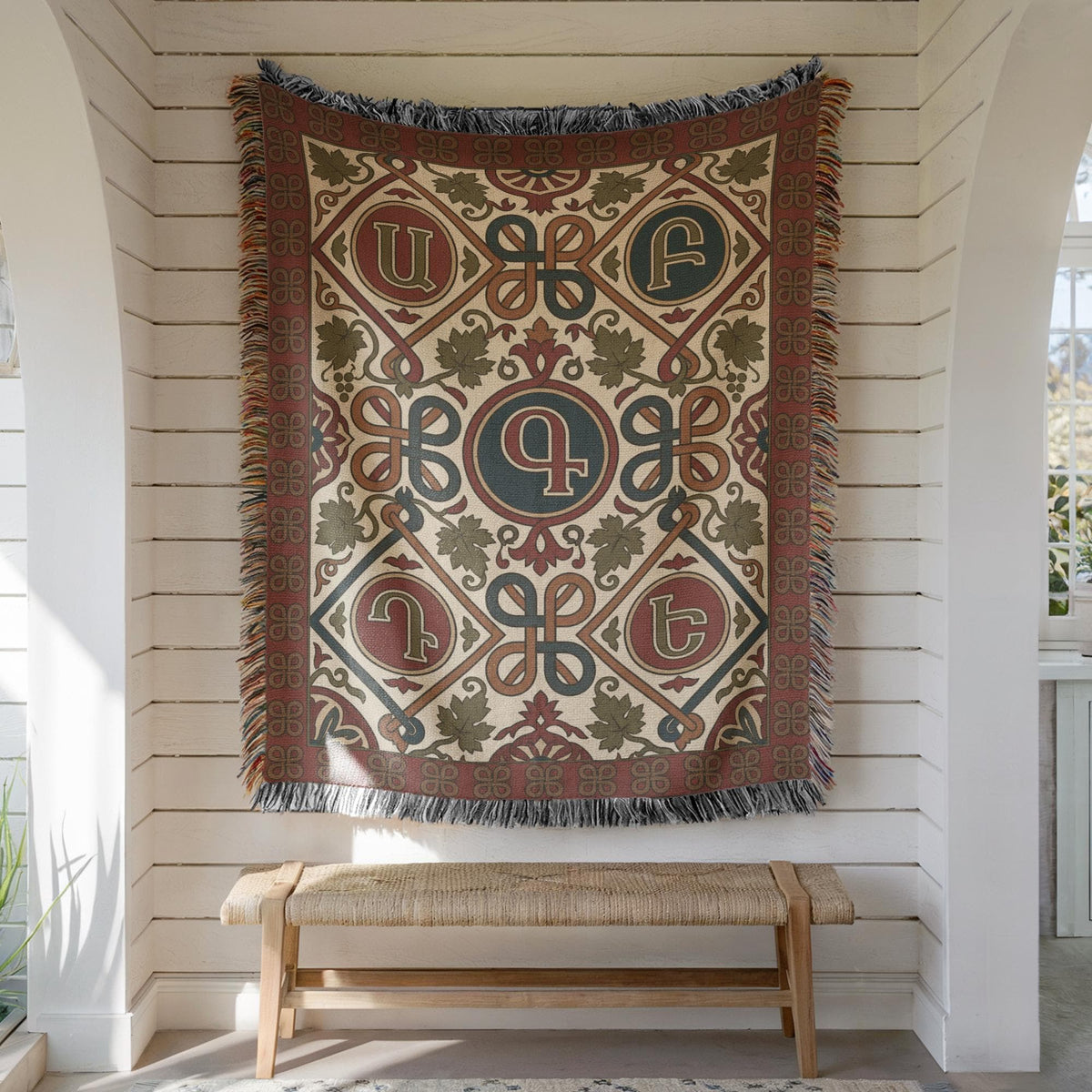 Armenian letter wall tapestry in rust and teal hung on white shiplap above a wooden bench