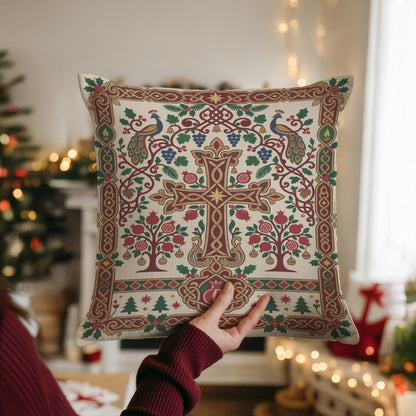 A person is holding up a decorative pillow with a cross and floral designs, with a Christmas tree and other holiday decorations visible in the background.