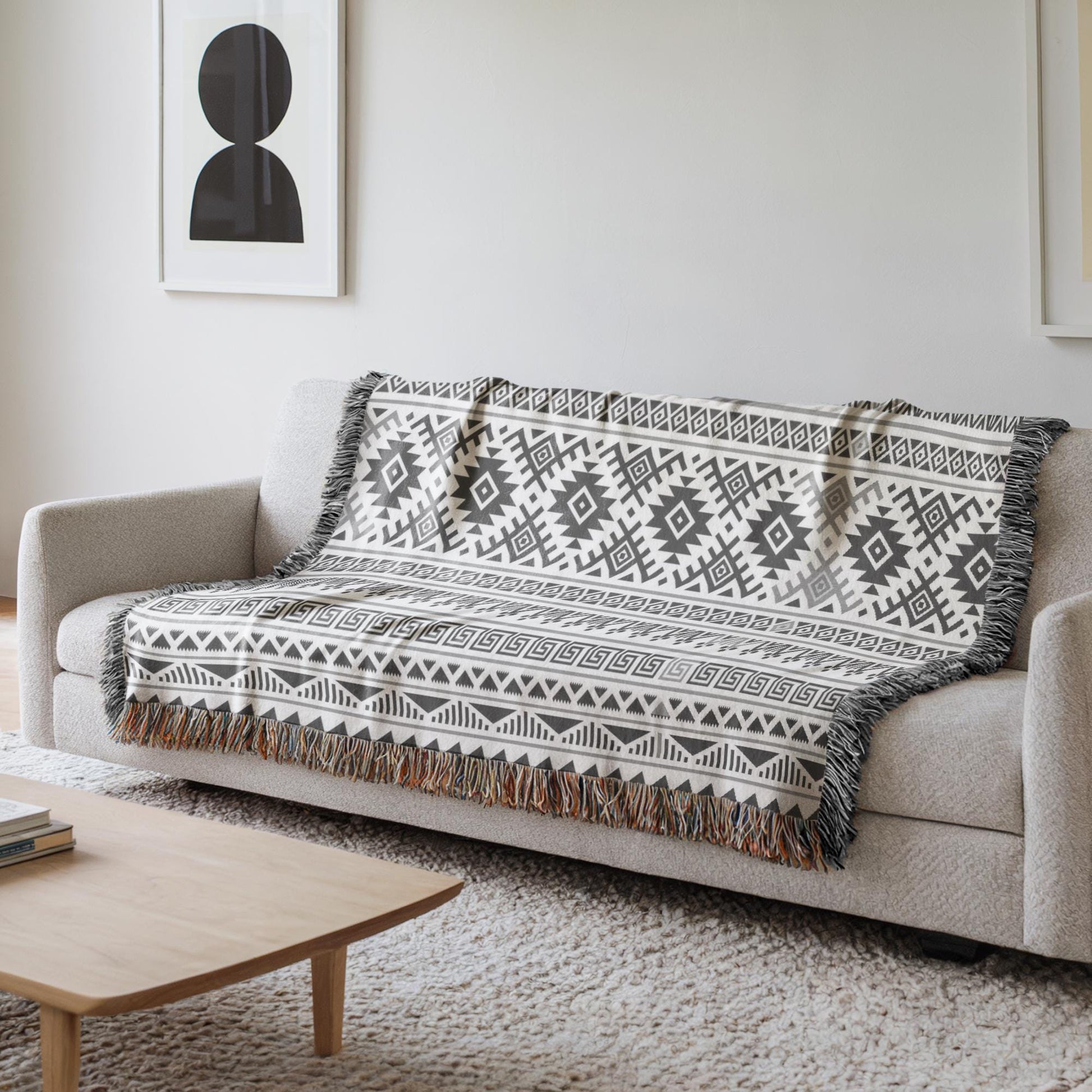 a cozy living room with a gray sofa adorned with a patterned throw blanket. The blanket has a geometric design in black and white, adding a touch of elegance to the space. In the background, there is a framed picture hanging on the wall, and a wooden coffee table is placed in front of the sofa.