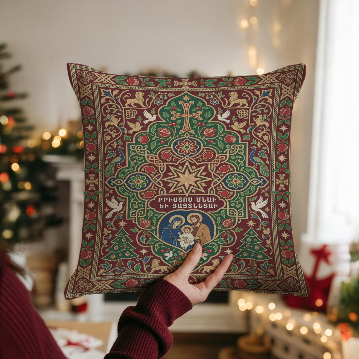 A person is holding up a pillow with a detailed, ornate design featuring a Christmas tree and religious imagery.