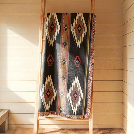 A colorful, patterned blanket is draped over a wooden ladder against a white wall.