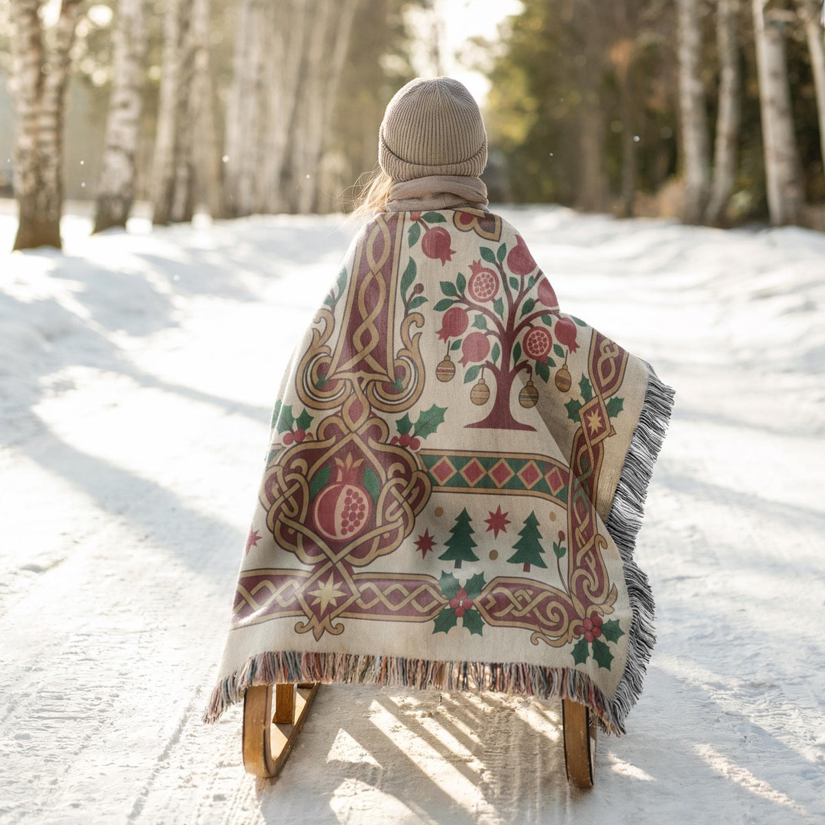A person is riding a sled down a snowy path, wearing a colorful blanket with a tree design.