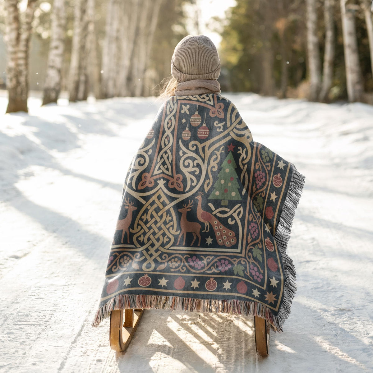 A person is riding a sled down a snowy path, wearing a colorful blanket with a pattern of deer and Christmas trees.