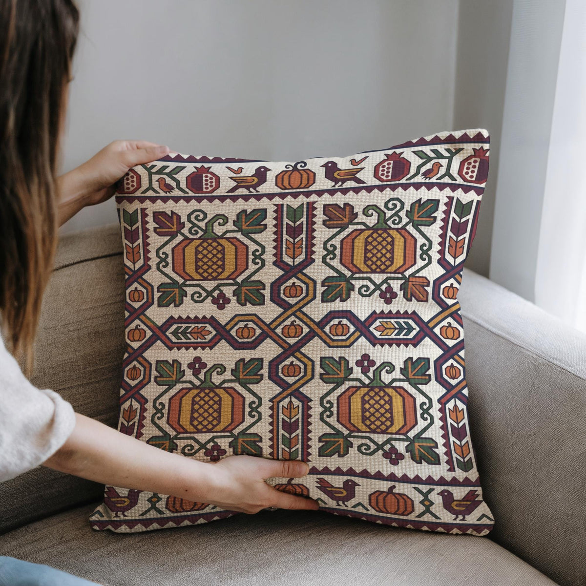 Hands placing the cream and gold Ghapama pillow onto a grey sofa